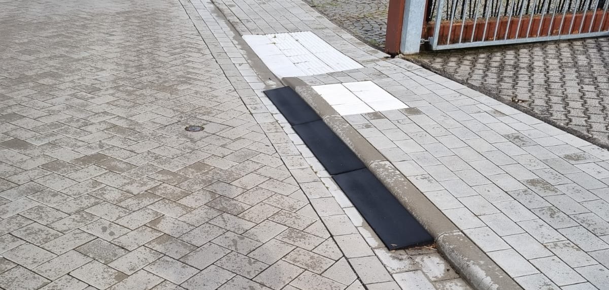 Gepflasterte Straße mit Bordsteinen und Überfahrhilfen in der Straßenrinne